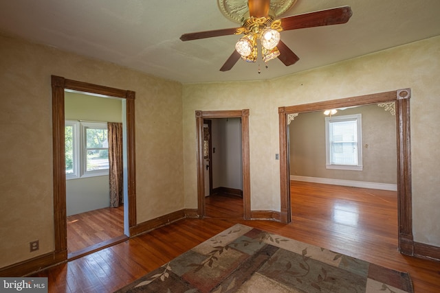 unfurnished bedroom featuring multiple windows, a ceiling fan, baseboards, and wood-type flooring