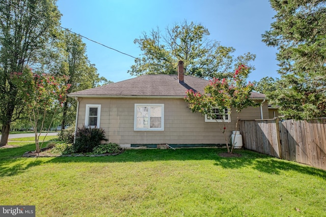 view of home's exterior with a shingled roof, a yard, fence, and a chimney