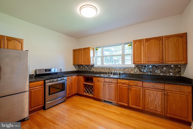 kitchen featuring brown cabinetry, a sink, decorative backsplash, light wood-style floors, and appliances with stainless steel finishes