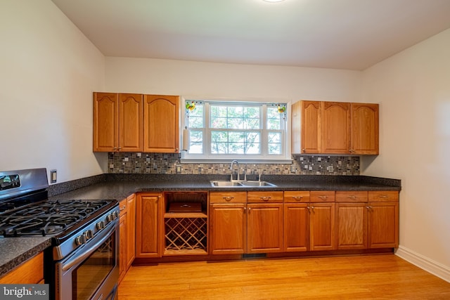 kitchen with a sink, dark countertops, brown cabinetry, and stainless steel gas range oven