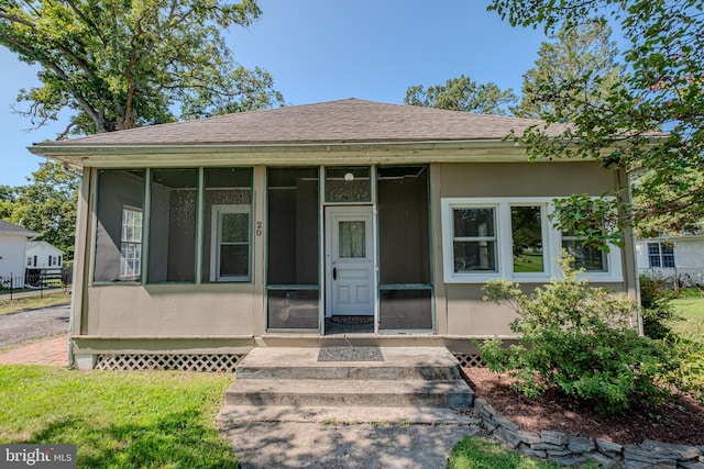 bungalow-style house with stucco siding, a shingled roof, and a sunroom