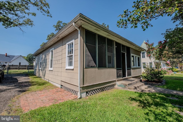 view of property exterior with a yard, fence, entry steps, and a sunroom