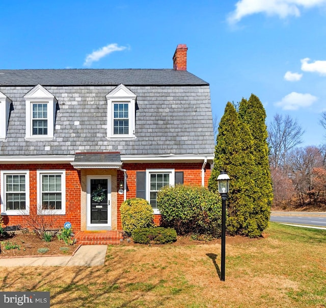 dutch colonial with brick siding, a high end roof, a chimney, and a front yard