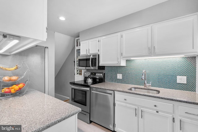 kitchen featuring a sink, light stone counters, tasteful backsplash, white cabinetry, and stainless steel appliances