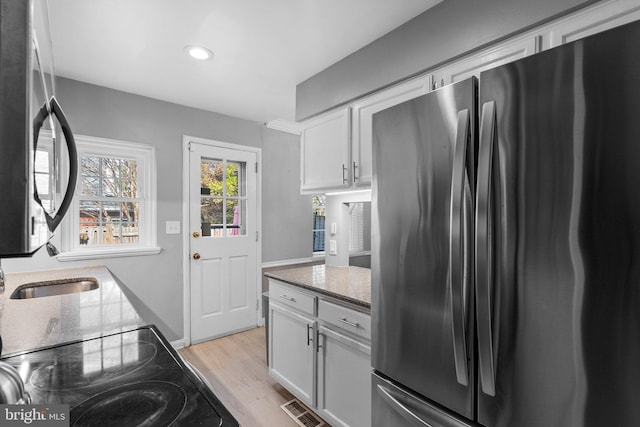 kitchen with light stone counters, visible vents, freestanding refrigerator, white cabinets, and light wood-style floors