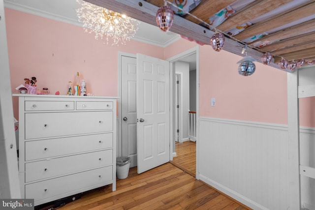 bedroom featuring a notable chandelier, a wainscoted wall, light wood-type flooring, and crown molding