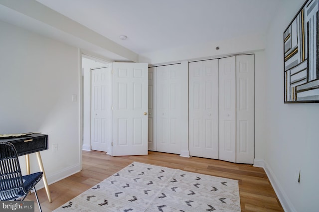 bedroom featuring baseboards, light wood-type flooring, and two closets