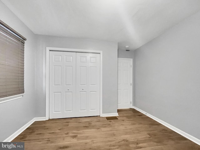 unfurnished bedroom featuring wood finished floors, baseboards, and a closet