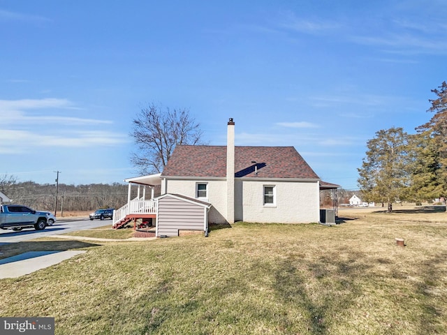 rear view of house featuring a chimney, central air condition unit, a shingled roof, and a yard