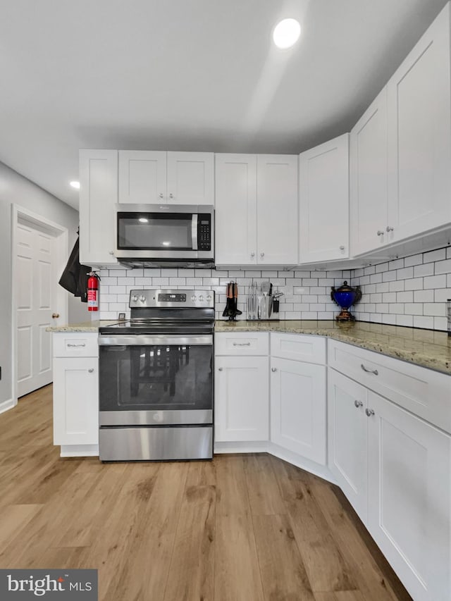 kitchen featuring light wood finished floors, light stone counters, decorative backsplash, appliances with stainless steel finishes, and white cabinetry