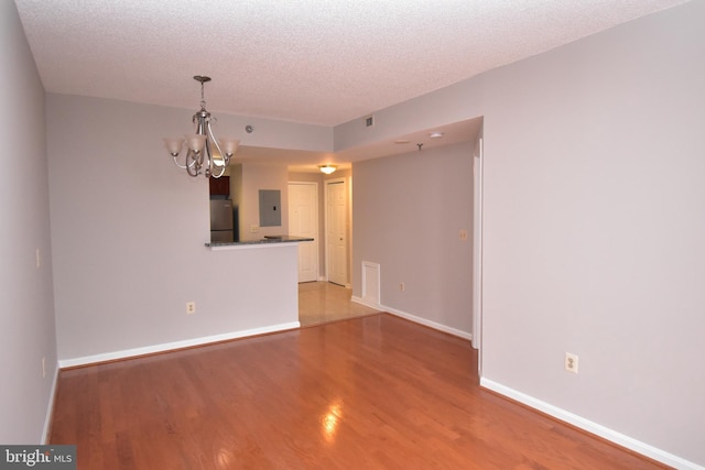 spare room featuring a textured ceiling, electric panel, wood finished floors, and a chandelier