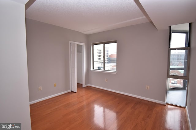 spare room featuring a textured ceiling, baseboards, and light wood-style floors