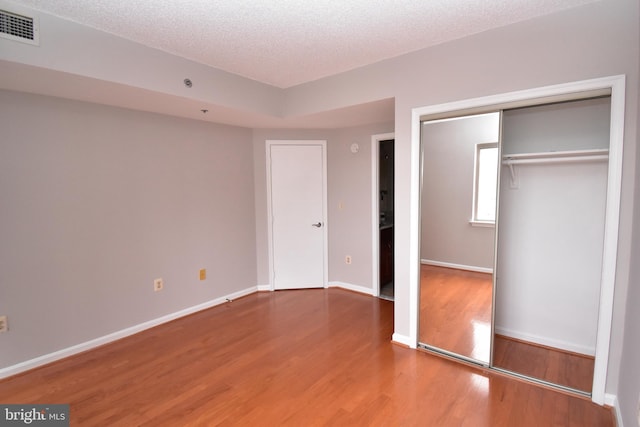 unfurnished bedroom featuring baseboards, wood finished floors, visible vents, and a textured ceiling