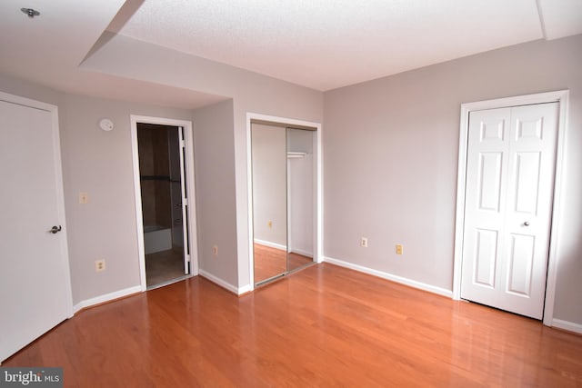 unfurnished bedroom featuring ensuite bath, two closets, baseboards, and wood finished floors