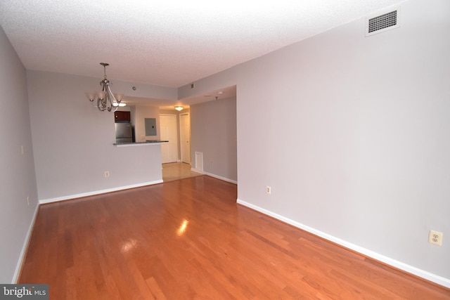 unfurnished living room with visible vents, a notable chandelier, a textured ceiling, light wood-style floors, and baseboards