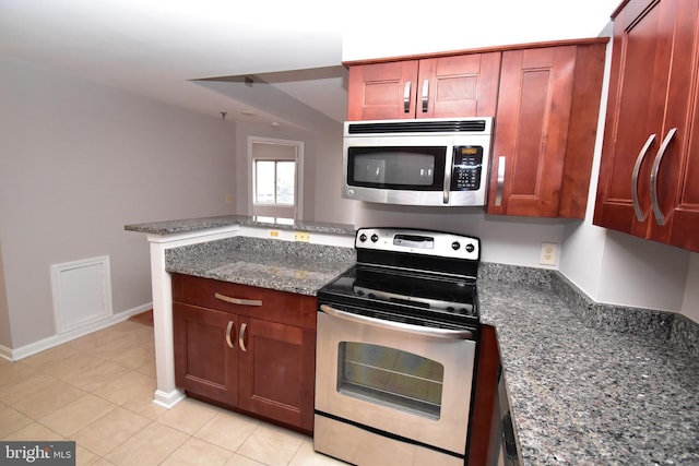 kitchen with baseboards, light tile patterned floors, dark stone countertops, a peninsula, and stainless steel appliances