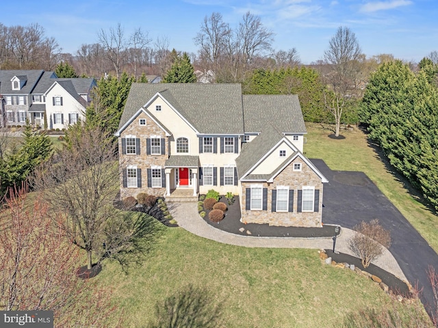 view of front of home with aphalt driveway, stone siding, and a front yard