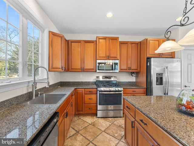 kitchen featuring brown cabinetry, dark stone countertops, appliances with stainless steel finishes, and a sink