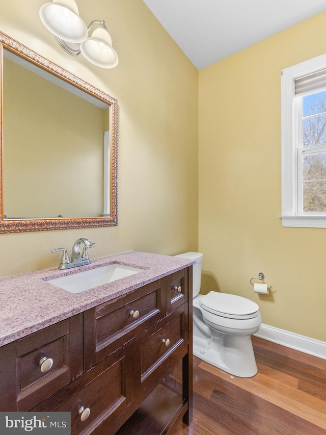 half bathroom featuring baseboards, toilet, wood finished floors, and vanity