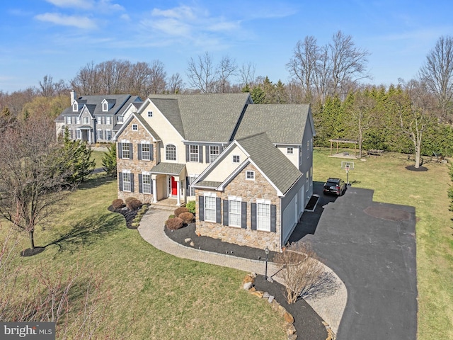 view of front of property featuring stone siding, a front lawn, driveway, and a shingled roof