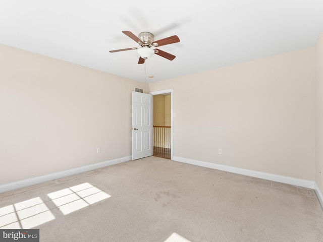 empty room with light colored carpet, a ceiling fan, and baseboards