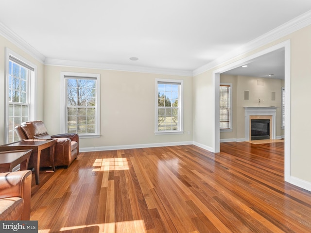 unfurnished room featuring a fireplace with flush hearth, wood finished floors, baseboards, and ornamental molding