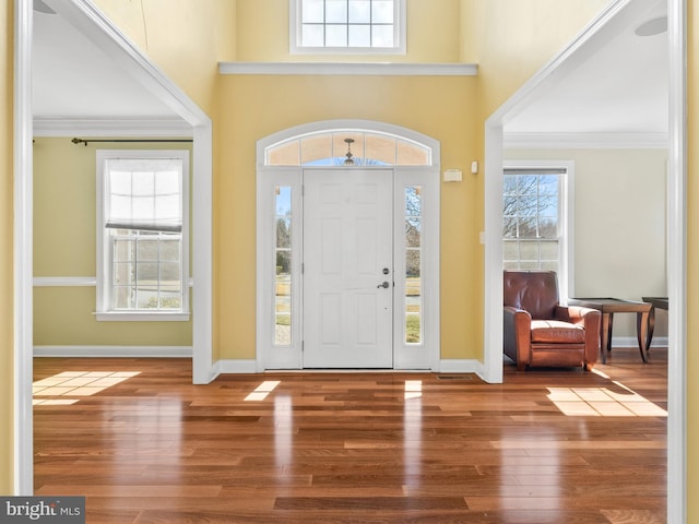 foyer entrance featuring a towering ceiling, crown molding, baseboards, and wood finished floors