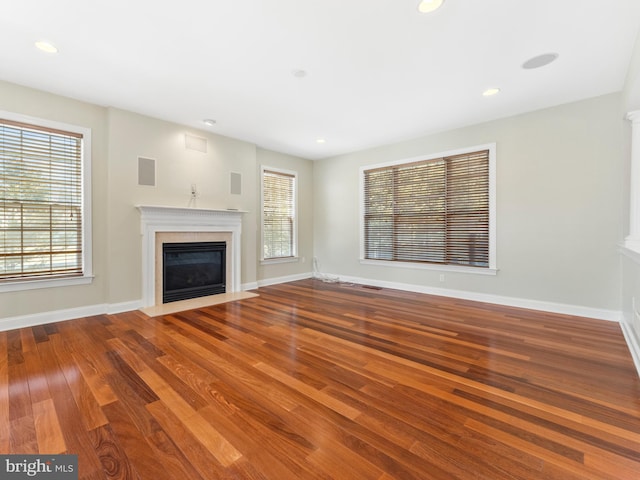 unfurnished living room with a fireplace with flush hearth, wood finished floors, visible vents, and baseboards