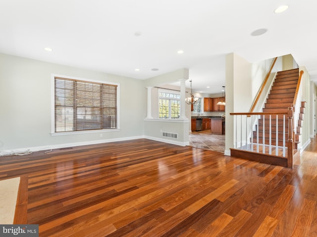 unfurnished living room featuring visible vents, baseboards, stairway, wood finished floors, and a notable chandelier