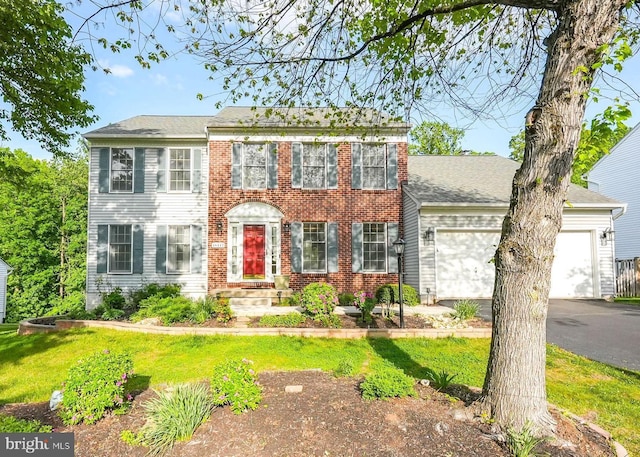 colonial inspired home with a garage, a front yard, brick siding, and aphalt driveway