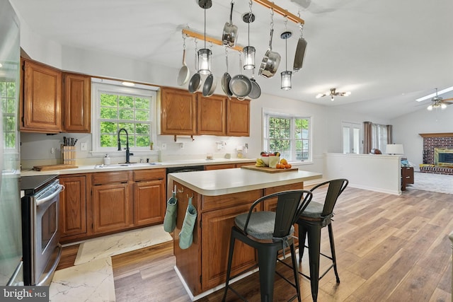 kitchen featuring a healthy amount of sunlight, light countertops, stainless steel electric range, brown cabinets, and a sink