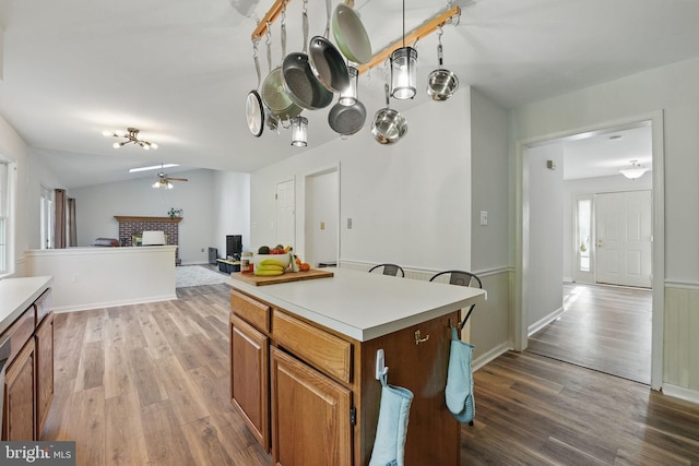 kitchen featuring a brick fireplace, ceiling fan, wood finished floors, and light countertops