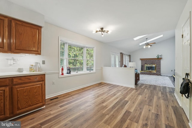 kitchen with visible vents, brown cabinetry, light wood finished floors, and a brick fireplace