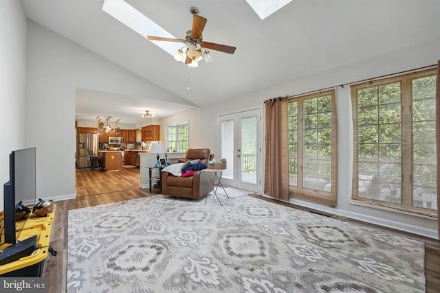 living area with ceiling fan, light wood-style floors, high vaulted ceiling, baseboards, and a skylight
