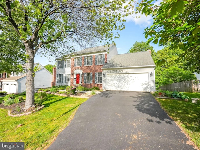 colonial inspired home featuring aphalt driveway, a garage, brick siding, fence, and a front lawn