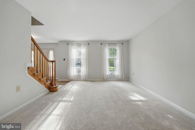 unfurnished living room featuring stairway, carpet floors, and baseboards