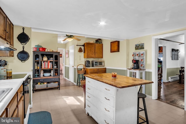 kitchen featuring a kitchen island, under cabinet range hood, light floors, a kitchen bar, and electric stove