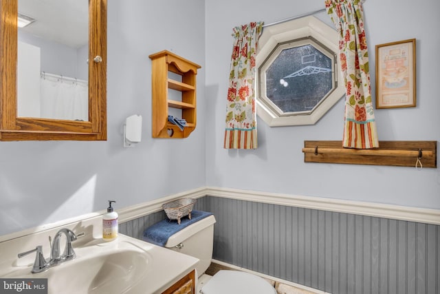 bathroom with vanity, toilet, and a wainscoted wall