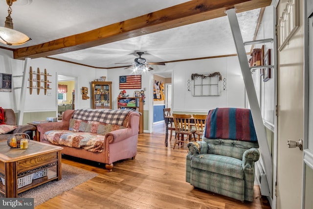 living room with beam ceiling, crown molding, a ceiling fan, and wood finished floors