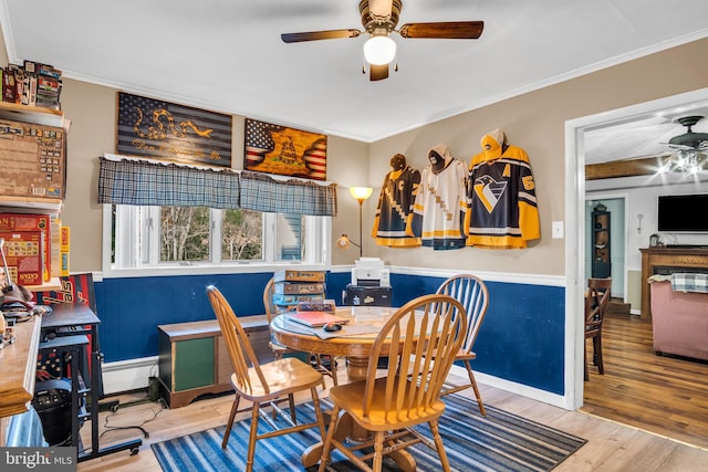 dining area with wainscoting, crown molding, a ceiling fan, and wood finished floors