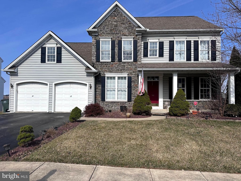 view of front facade featuring a front yard, driveway, covered porch, a garage, and stone siding