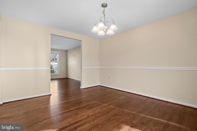 empty room featuring wood finished floors, baseboards, and a chandelier