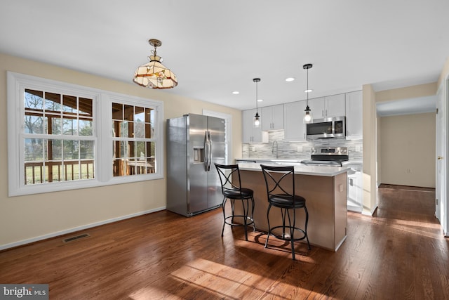 kitchen with decorative backsplash, a kitchen island, appliances with stainless steel finishes, and dark wood-style floors