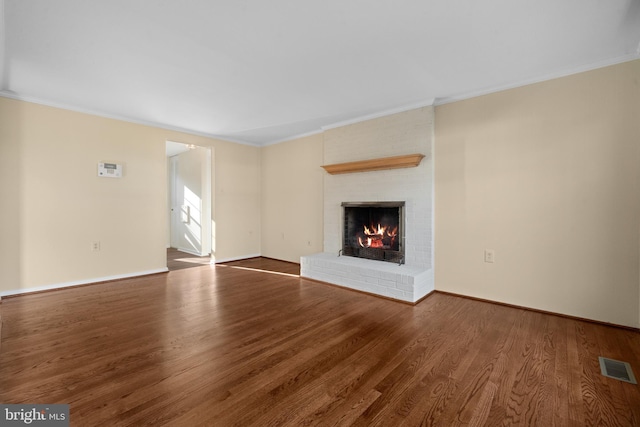 unfurnished living room featuring visible vents, wood finished floors, crown molding, baseboards, and a brick fireplace