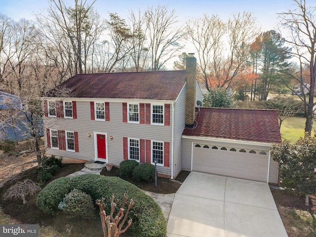 view of front facade featuring a shingled roof, an attached garage, driveway, and a chimney