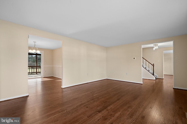 unfurnished room featuring a chandelier, stairway, dark wood finished floors, and baseboards