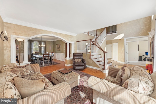 living area featuring wood finished floors, ornate columns, arched walkways, ornamental molding, and stairs