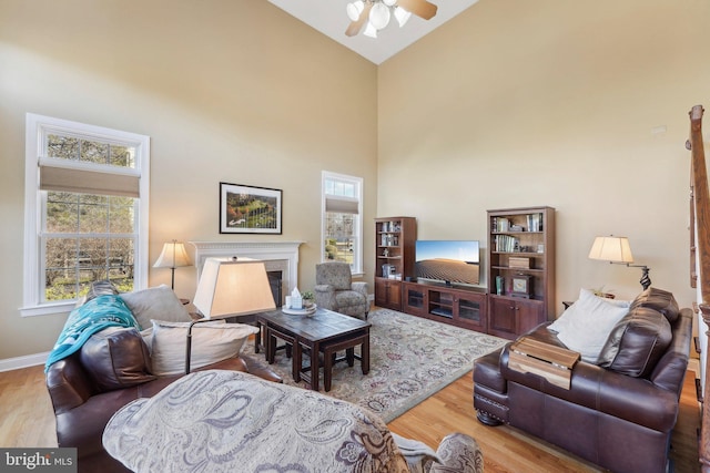 living area featuring high vaulted ceiling, a ceiling fan, wood finished floors, a high end fireplace, and baseboards