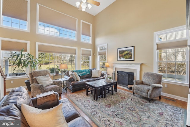 living area featuring visible vents, ceiling fan, baseboards, a fireplace, and wood finished floors