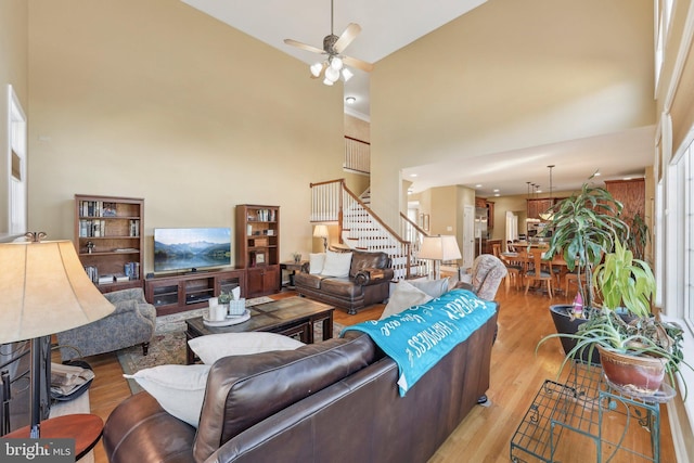 living room featuring stairway, light wood-style floors, a high ceiling, and ceiling fan